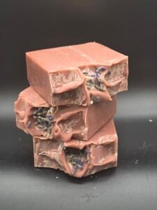 Jabón artesanal rosa polvoriento de arcilla morada con leche de coco y aceites esenciales de lavanda y limón, decorado con lavanda seca en la superficie.