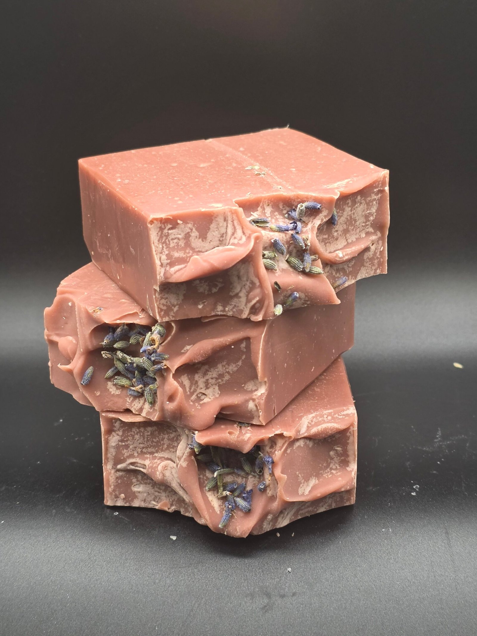 Jabón artesanal rosa polvoriento de arcilla morada con leche de coco y aceites esenciales de lavanda y limón, decorado con lavanda seca en la superficie.